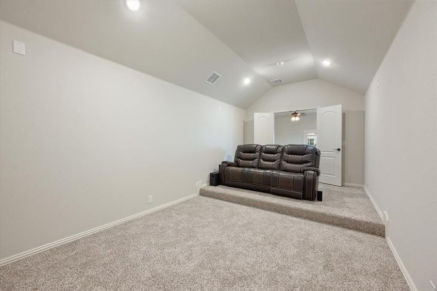 Carpeted home theater room with stadium seating and a vaulted ceiling with recessed lighting. French doors lead into the game room.