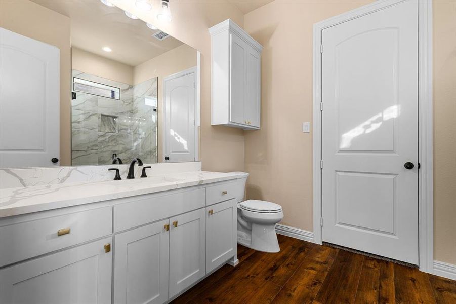 Bathroom featuring hardwood / wood-style flooring, vanity, toilet, and a tile shower