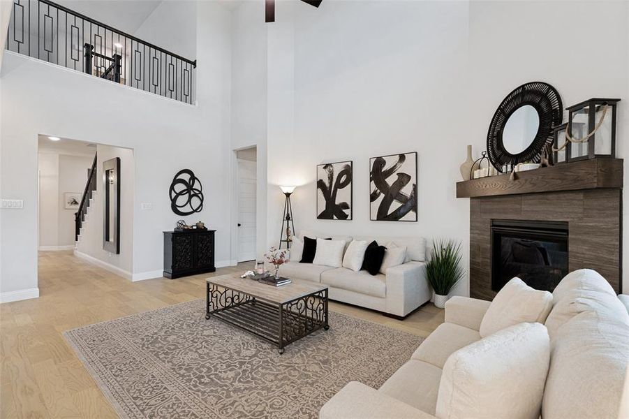 Two-story living area featuring light wood-finish flooring, a contemporary fireplace with a wood mantel, a second-story open hallway with black metal railing, and high ceilings