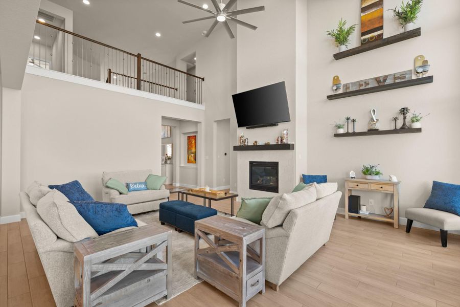 Living area featuring light wood finished floors, a towering ceiling, ceiling fan, a glass covered fireplace, and recessed lighting Living area featuring light wood finished floors, a towering ceiling, ceiling fan, a glass covered fireplace, and recessed lighting