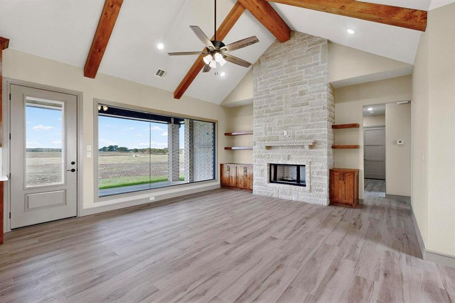 Unfurnished living room featuring high vaulted ceiling, light wood-type flooring, recessed lighting, beam ceiling, and a stone fireplace Unfurnished living room featuring high vaulted ceiling, light wood-type flooring, recessed lighting, beam ceiling, and a stone fireplace