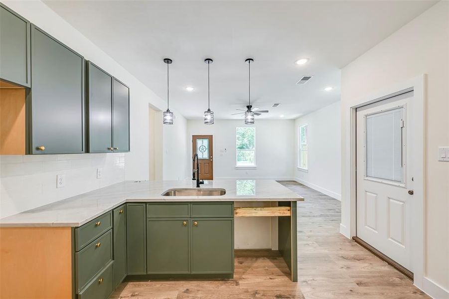 Kitchen island featuring an undermount sink, three pendant lights, and a light-toned countertop Kitchen island featuring an undermount sink, three pendant lights, and a light-toned countertop