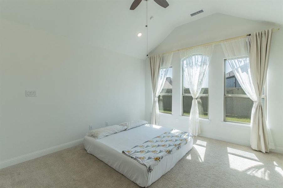Vaulted ceiling bedroom with three arched windows, soft neutral carpet, a ceiling fan, and white baseboards