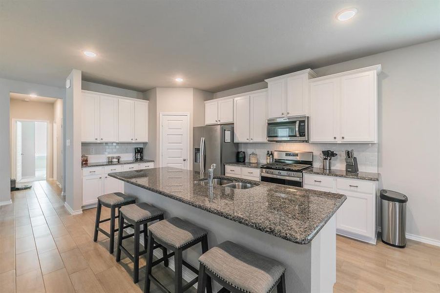 Kitchen with a kitchen bar, appliances with stainless steel finishes, decorative backsplash, white cabinetry, and dark stone countertops