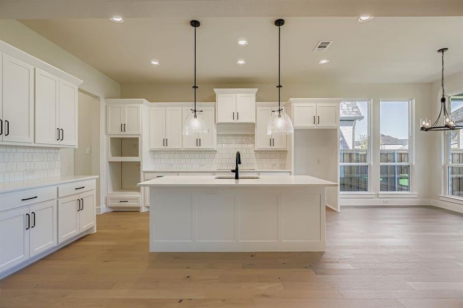 Kitchen with recessed lighting, white cabinetry, pendant lighting, an island with sink, and light stone countertops