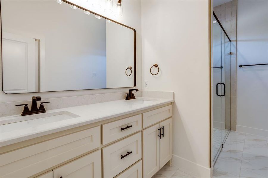 Bathroom featuring double vanity, a stall shower, and light marble finish floors