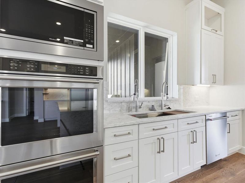 Kitchen featuring appliances with stainless steel finishes, white cabinetry, glass insert cabinets, light stone countertops, and dark wood-type flooring Kitchen featuring appliances with stainless steel finishes, white cabinetry, glass insert cabinets, light stone countertops, and dark wood-type flooring