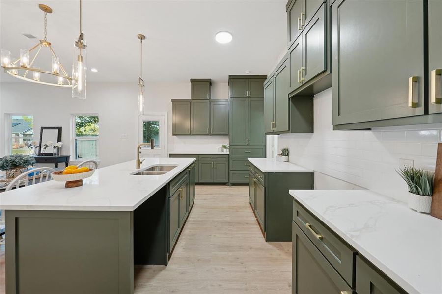 Kitchen with green cabinetry, decorative backsplash, light wood-style flooring, light stone counters, and a center island with sink