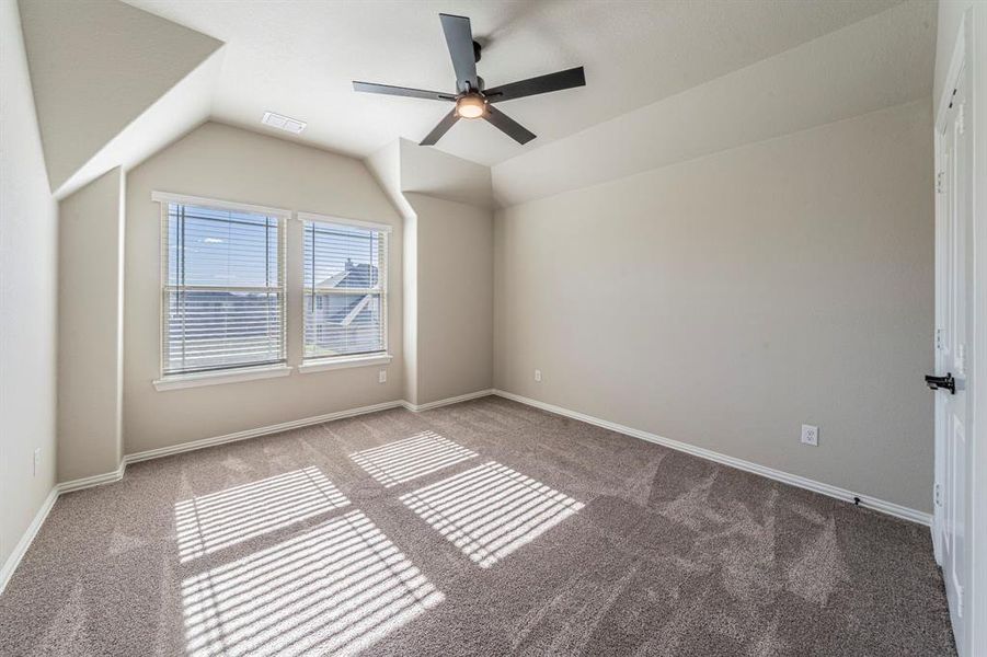 Spacious room featuring vaulted ceilings, two large windows with blinds, plush gray carpeting, a contemporary ceiling fan with integrated lighting, and neutral wall tones