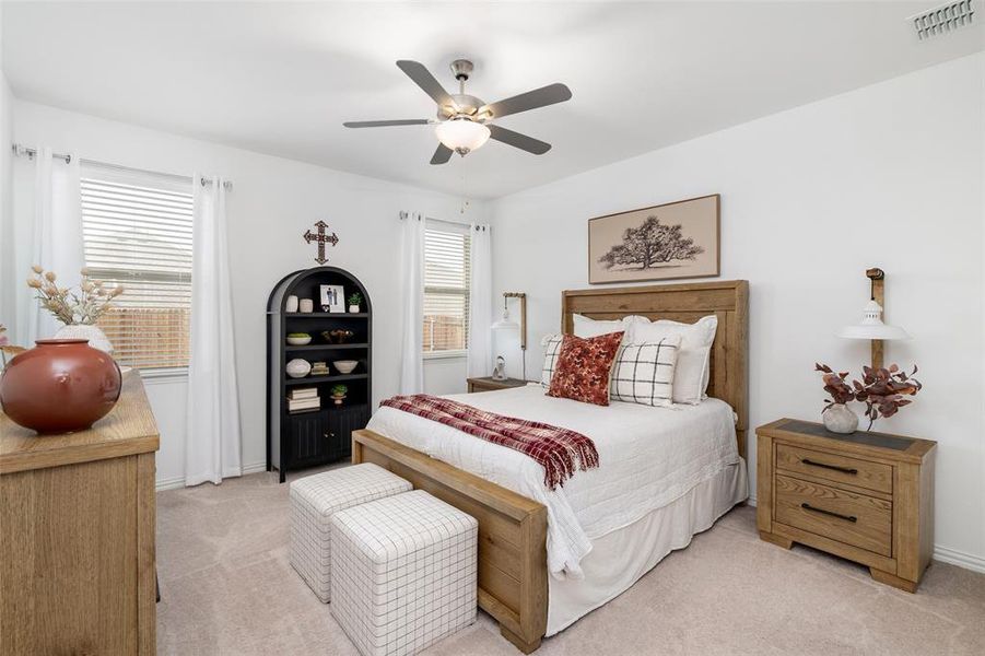 This bedroom features light-colored carpeting, a ceiling fan, and windows with blinds and white curtains
