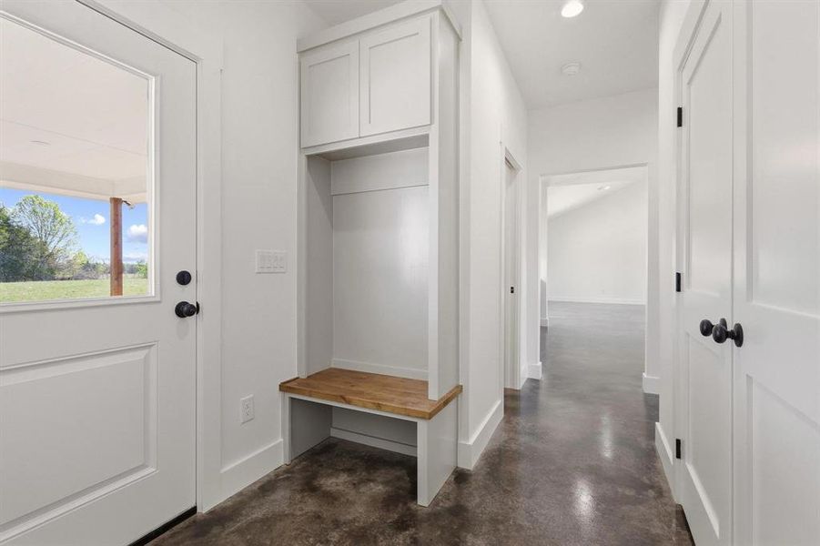 Entryway featuring a built-in bench with storage, a white door with a clear glass panel, and polished concrete flooring