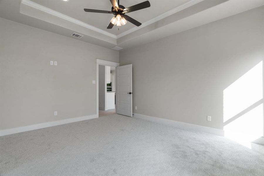 Unfurnished bedroom with crown molding, light carpet, multiple windows, a tray ceiling, and ceiling fan