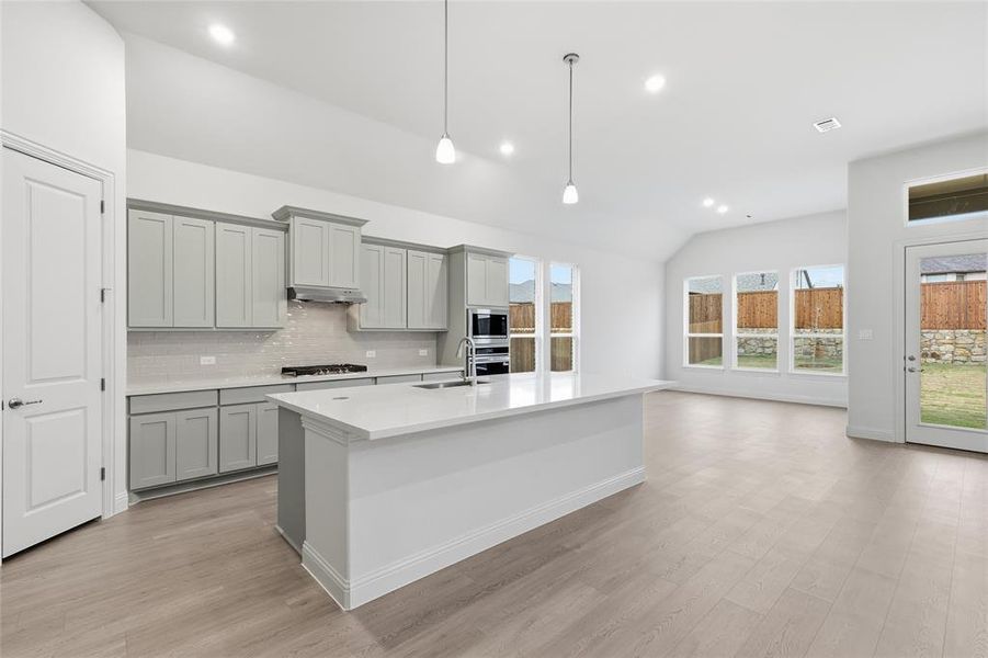 Kitchen with vaulted ceiling, gray cabinets, light wood finished floors, tasteful backsplash, and decorative light fixtures