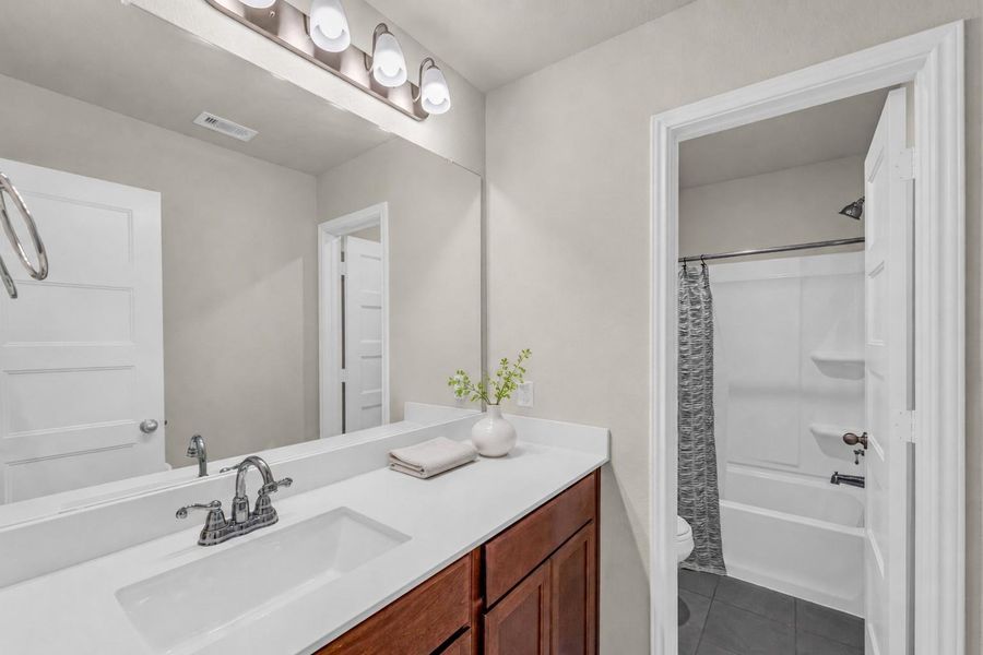 A well-lit full bathroom includes a long vanity with an under-mount sink, large mirror, and an adjoining private tub-shower combination. A well-lit full bathroom includes a long vanity with an under-mount sink, large mirror, and an adjoining private tub-shower combination.