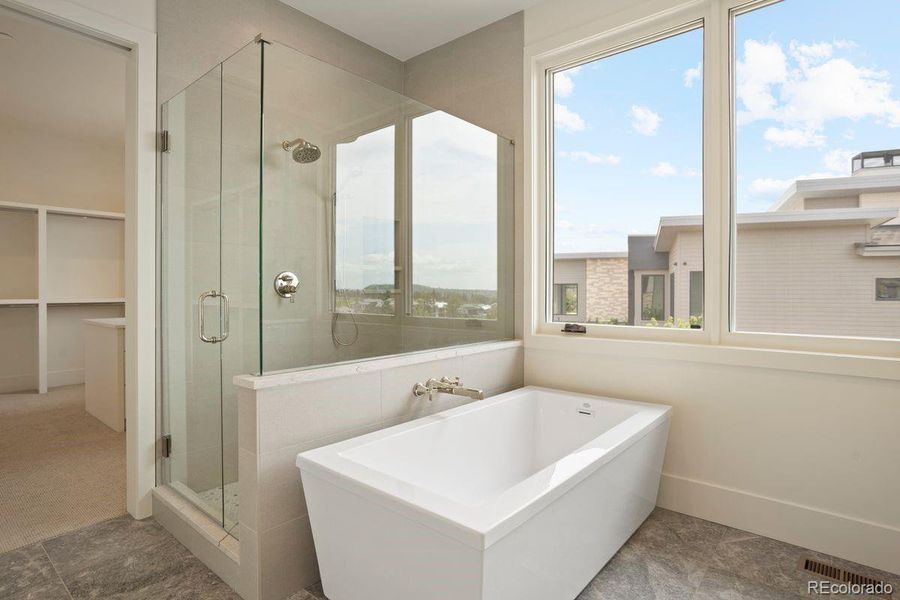 Primary bath with a frameless glass shower, freestanding soaking tub, and access to the large primary closet.
