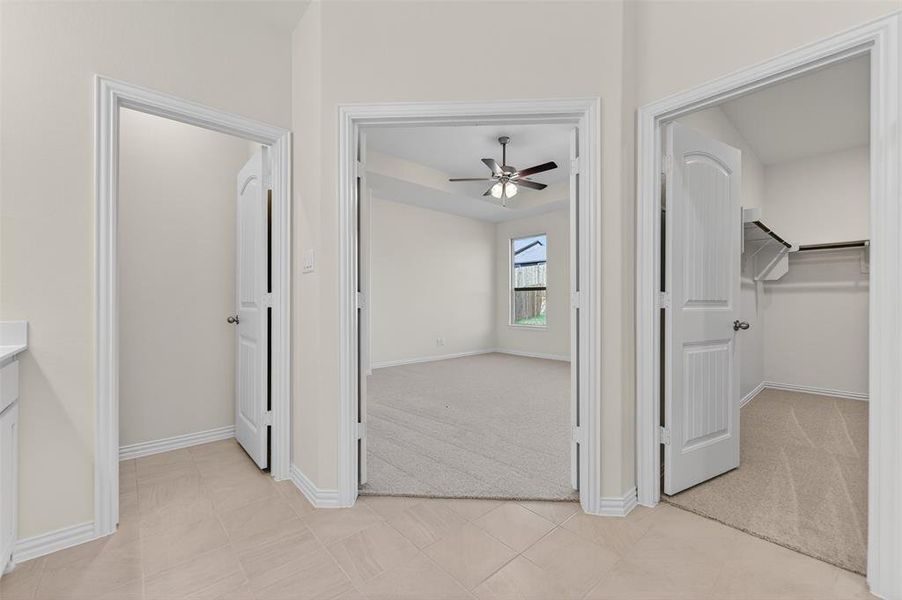 Unfurnished bedroom featuring a spacious closet, light carpet, light tile patterned flooring, and ceiling fan