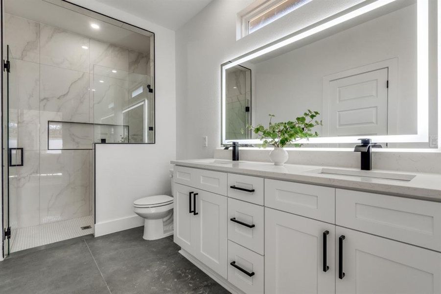 Bathroom with toilet, a sink, a marble finish shower, and double vanity