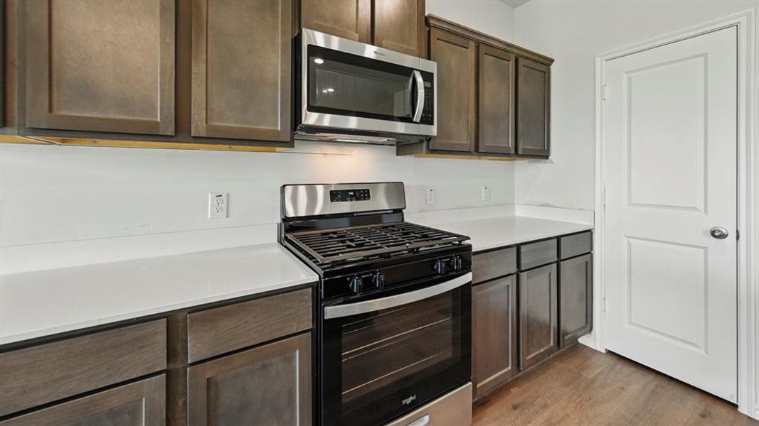 Kitchen featuring appliances with stainless steel finishes, dark brown cabinets, dark wood-style floors, and light stone counters