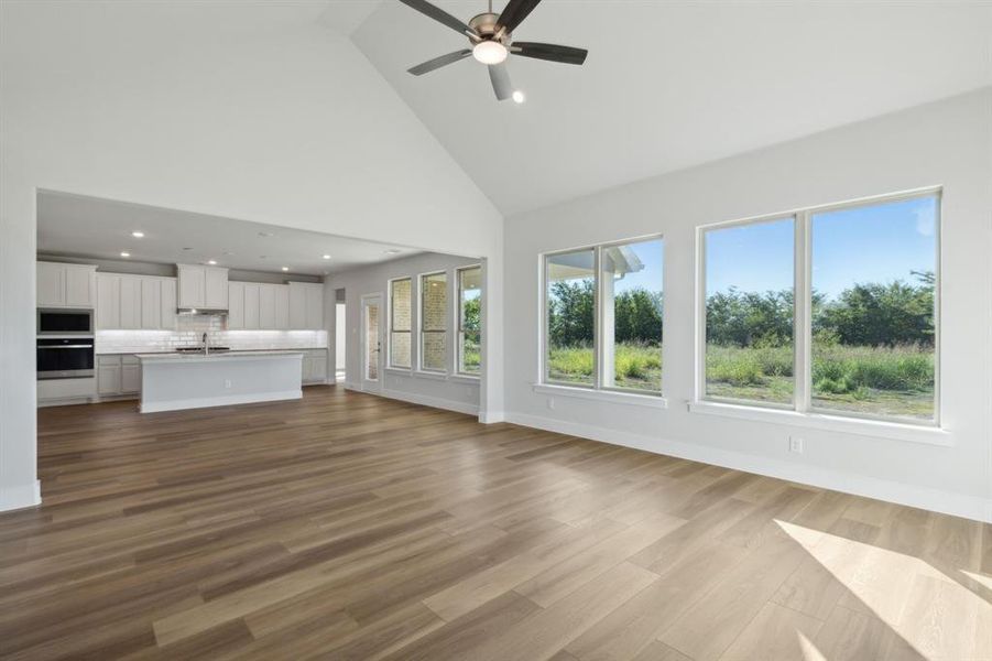 Unfurnished living room featuring ceiling fan, high vaulted ceiling, sink, and light wood-type flooring