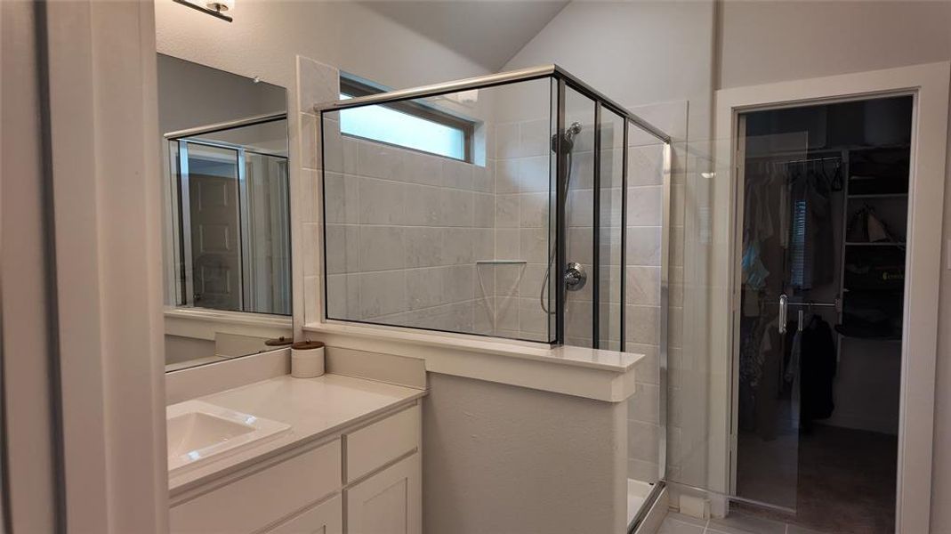 Bathroom featuring a vanity with an integrated sink, a large mirror, and a glass-enclosed shower with tile walls