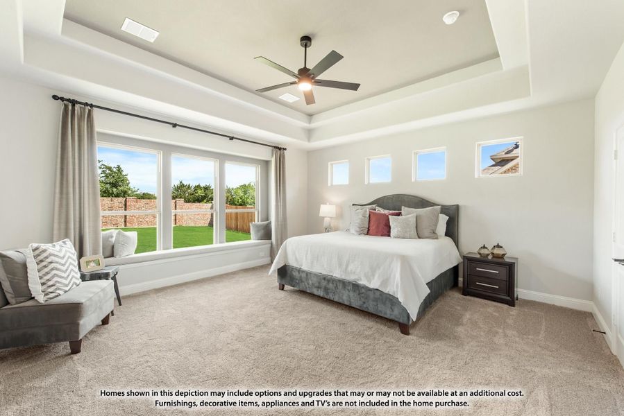 Spacious master bedroom with tray ceiling, ceiling fan, window seat, and large windows overlooking backyard