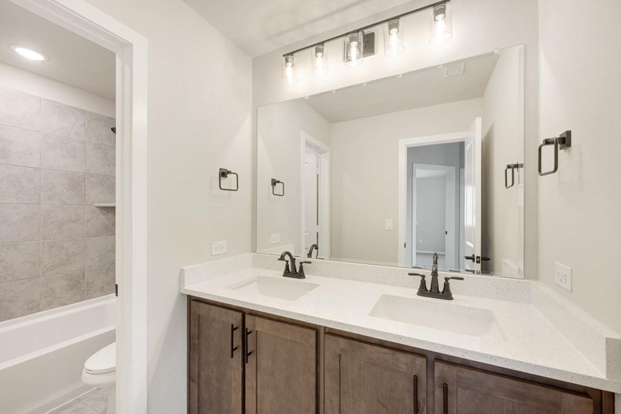 Bathroom with double sink vanity, dark wood cabinets, white quartz countertop, and tiled shower-tub combo