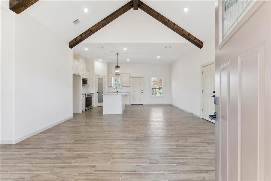 Unfurnished living room featuring beam ceiling, high vaulted ceiling, and light hardwood / wood-style flooring