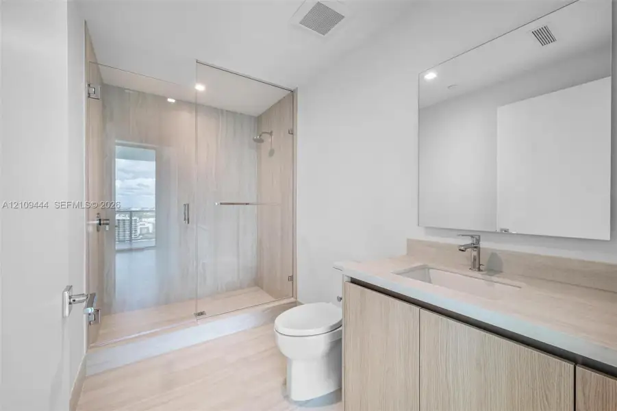 Bathroom featuring wood-finish cabinetry, a large integrated mirror, a walk-in shower with a glass enclosure and floor-to-ceiling wall tile, and light-toned flooring