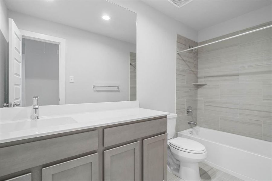 Secondary bath features tile flooring, bath/shower combo with tile surround, stained wood cabinets, beautiful light countertops, mirror, sleek fixtures and modern finishes.