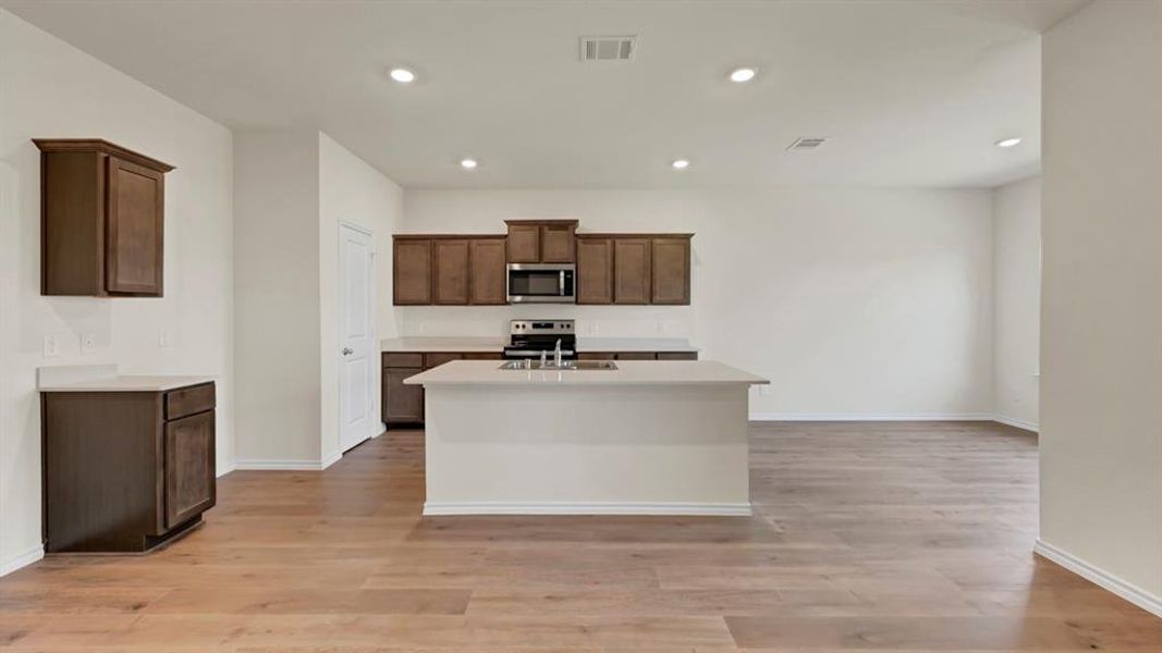 Open-concept kitchen featuring an island, wood-finish flooring, recessed lighting, white walls, and dark wood cabinetry with light countertops