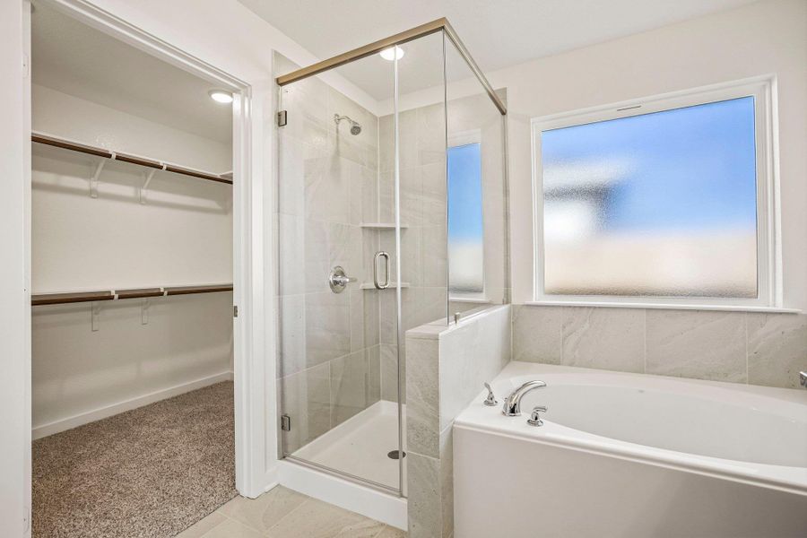 An inviting soaking tub and glass shower stand adjacent to a walk-in closet.