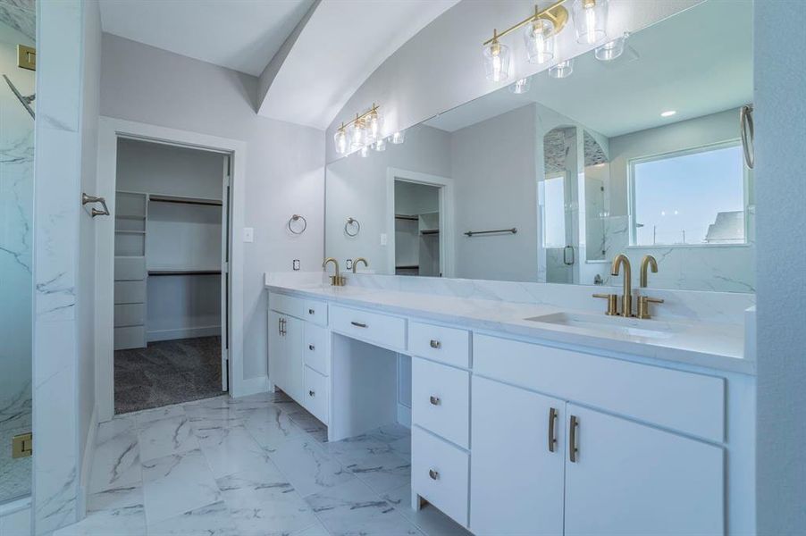 Full bathroom featuring a spacious closet, a marble finish shower, light marble finish flooring, and double vanity