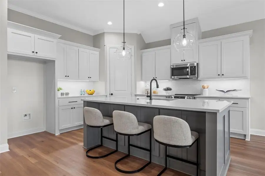 Kitchen featuring white cabinets, a breakfast bar, tasteful backsplash, stainless steel microwave, and recessed lighting Kitchen featuring white cabinets, a breakfast bar, tasteful backsplash, stainless steel microwave, and recessed lighting