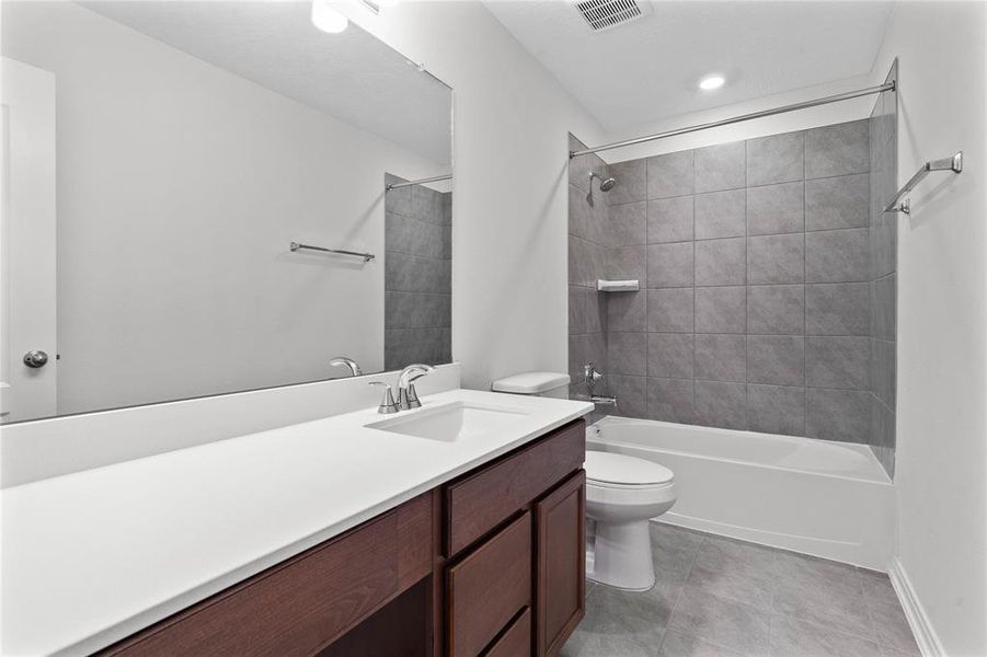 Secondary bath features tile flooring, bath/shower combo with tile surround, stained wood cabinets, beautiful light countertops, mirror, sleek and modern finishes.