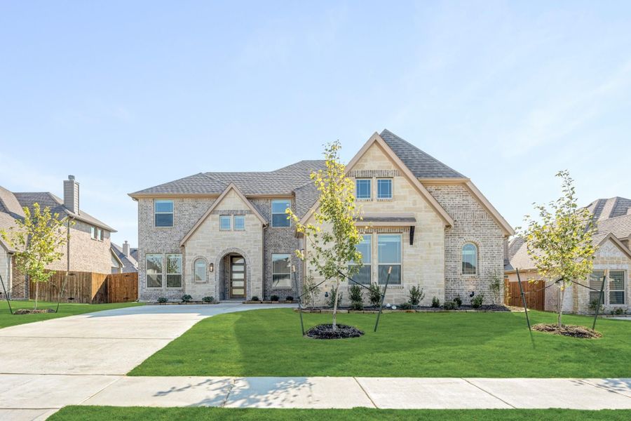 Two-story home with brick and stone exterior, arched entry, and manicured front lawn with young trees