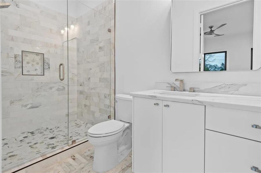 Bathroom featuring a glass-enclosed shower with tiled walls and floor, a white vanity with a countertop, a rectangular mirror, and a modern toilet Bathroom featuring a glass-enclosed shower with tiled walls and floor, a white vanity with a countertop, a rectangular mirror, and a modern toilet