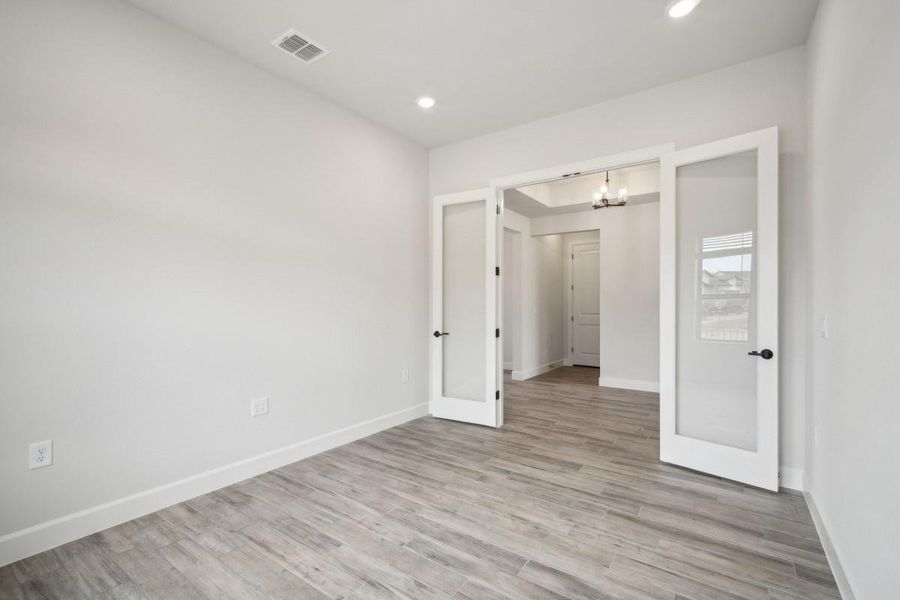 Empty room featuring light wood-type flooring, baseboards, visible vents, recessed lighting, and an inviting chandelier Empty room featuring light wood-type flooring, baseboards, visible vents, recessed lighting, and an inviting chandelier