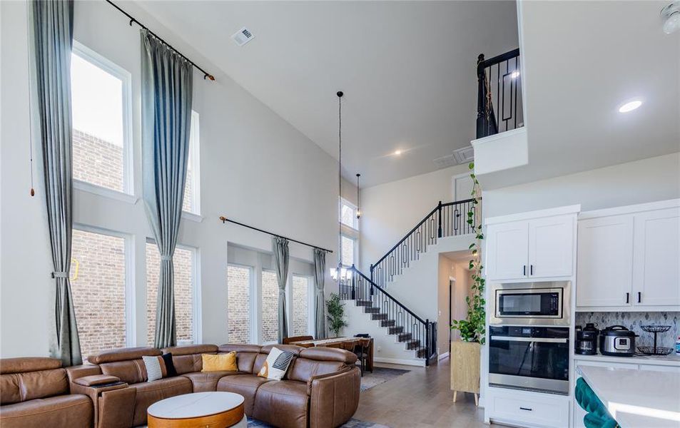 Living room featuring a towering ceiling, light wood-type flooring, and stairs
