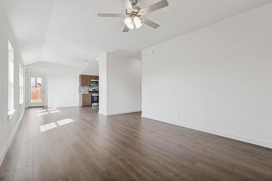 Unfurnished living room with vaulted ceiling, dark hardwood / wood-style floors, and ceiling fan