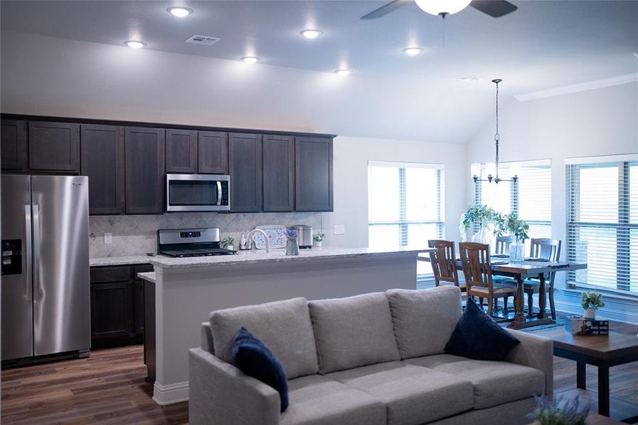 Kitchen with ceiling fan with notable chandelier, stainless steel appliances, light stone countertops, decorative backsplash, and dark wood-type flooring