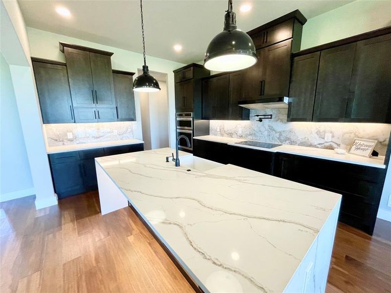 Kitchen featuring an island with sink, pendant lighting, decorative backsplash, and dark hardwood / wood-style flooring