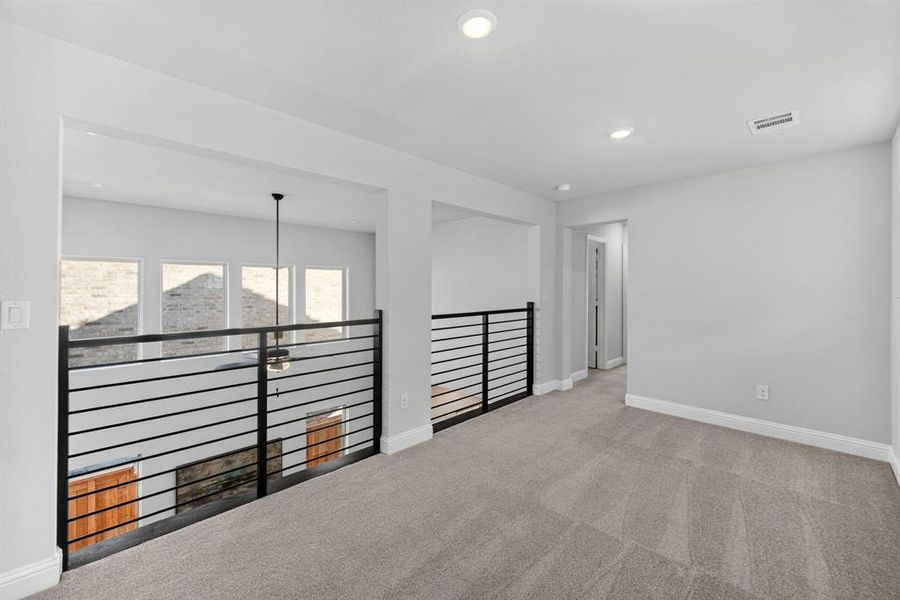 Carpeted loft space featuring contemporary black horizontal railings and white trim