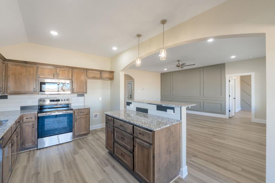Kitchen with stainless steel appliances, light stone countertops, hanging light fixtures, a kitchen island, and arched walkways