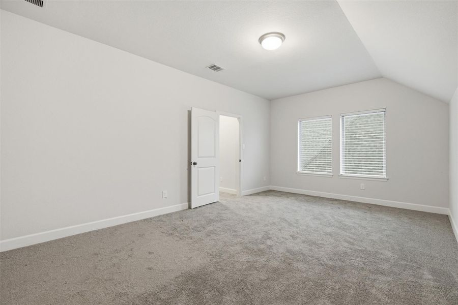 This photo shows a spacious bedroom with neutral walls and carpet, featuring two windows providing natural light. There's a door leading to an adjoining room or closet. The ceiling is equipped with a modern light fixture. This photo shows a spacious bedroom with neutral walls and carpet, featuring two windows providing natural light. There's a door leading to an adjoining room or closet. The ceiling is equipped with a modern light fixture.
