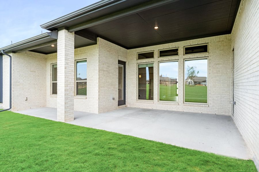 Covered back patio with concrete floor, white brick exterior, large windows, and green lawn Covered back patio with concrete floor, white brick exterior, large windows, and green lawn