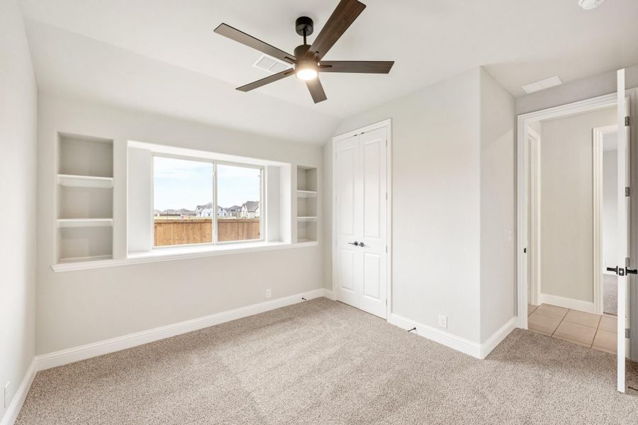 Empty bedroom with carpet, ceiling fan, built-in shelves beside window, and closet door Empty bedroom with carpet, ceiling fan, built-in shelves beside window, and closet door