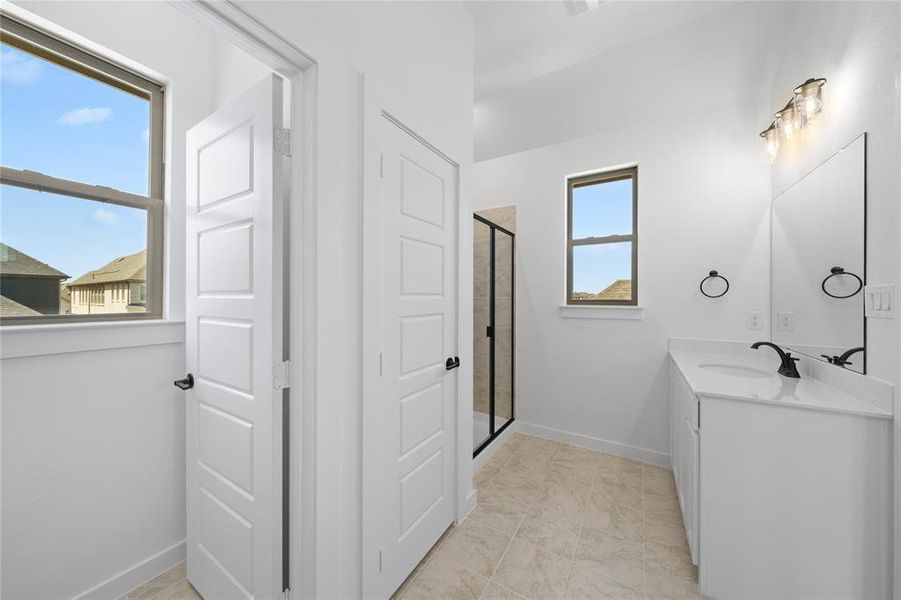 Bathroom featuring a glass-enclosed shower, single vanity with a white countertop, large mirror, and neutral tile flooring