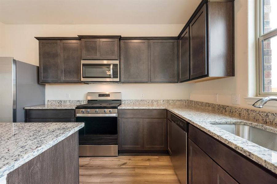 Kitchen featuring a healthy amount of sunlight, light hardwood / wood-style flooring, appliances with stainless steel finishes, and light stone countertops