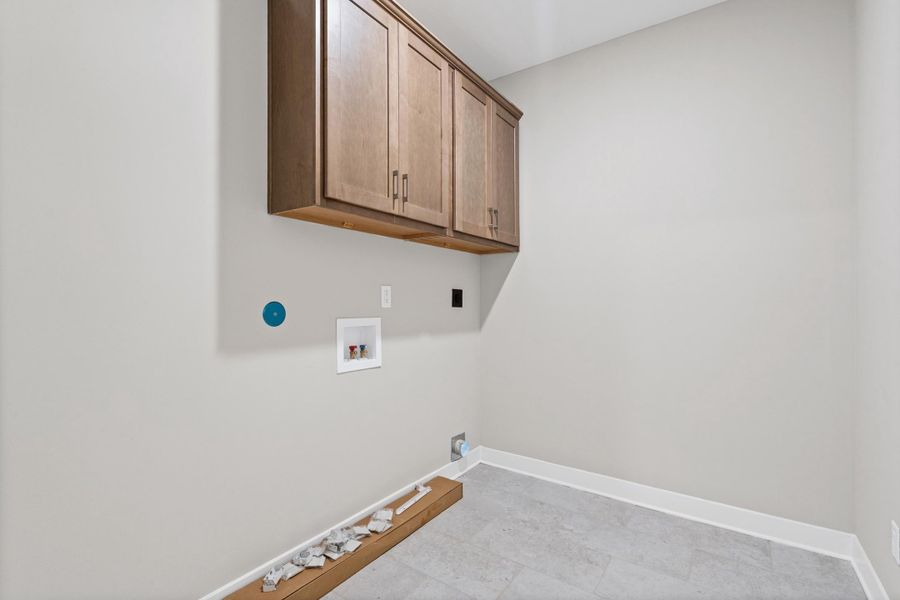 Laundry area featuring wood-finish cabinetry, light grey wall paint, and grey tile flooring Laundry area featuring wood-finish cabinetry, light grey wall paint, and grey tile flooring