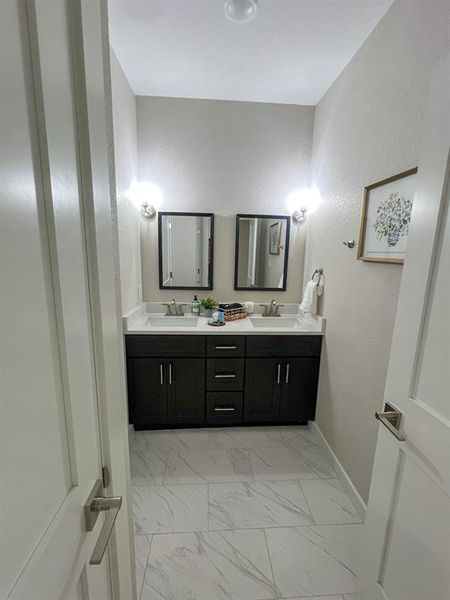 Full bathroom featuring light marble finish floors, double vanity, and a textured wall